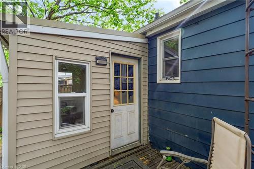 Exterior features include tan horizontal siding, a white-framed window, and a white exterior door with glass inserts - 703 Brighton Avenue, Hamilton, ON - Outdoor With Exterior