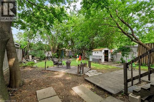 Expansive backyard featuring mature trees, a wood deck, a storage shed, a fire pit area, and a grassy lawn - 703 Brighton Avenue, Hamilton, ON - Outdoor