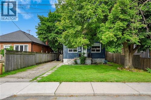 Blue siding exterior with white trim, mature front yard tree, concrete front walk, and a paved driveway - 703 Brighton Avenue, Hamilton, ON - Outdoor