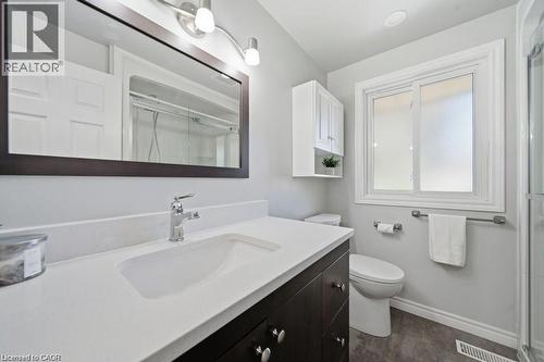 White vanity with integrated sink and chrome faucet, wood-finish flooring, and white-framed window - 64 Warren Road, Kitchener, ON - Indoor Photo Showing Bathroom