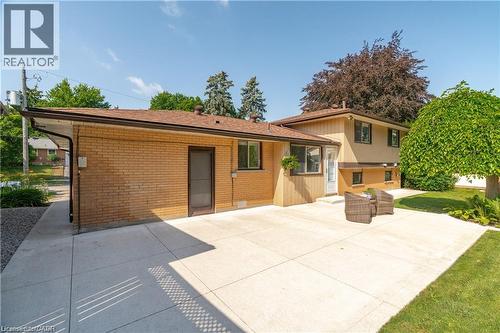 Expansive concrete patio with direct exterior access, complemented by a manicured lawn and mature landscaping - 64 Warren Road, Kitchener, ON - Outdoor