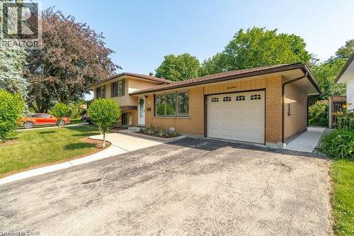 Brick-clad exterior with a garage, mature trees, and a concrete pathway leading to the entrance - 64 Warren Road, Kitchener, ON - Outdoor