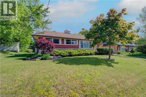 Red brick exterior with white trim, a brown shingle roof, front garden beds, mature trees, and a spacious green lawn - 251 Union Street E, Waterloo, ON - Outdoor