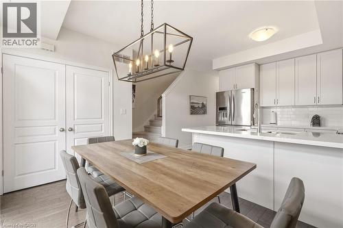 Open-concept dining and kitchen space featuring a modern chandelier, white flat-panel cabinetry, stainless steel appliances, and a white subway tile backsplash - 4171 Palermo Common, Burlington, ON - Indoor