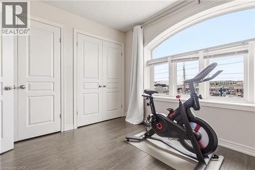 Bright corner bedroom showcasing expansive arched windows framing panoramic city vistas, rich wood-finish flooring, and crisp white six-panel closet doors with polished hardware - 4171 Palermo Common, Burlington, ON - Indoor Photo Showing Gym Room