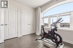 Bright corner bedroom showcasing expansive arched windows framing panoramic city vistas, rich wood-finish flooring, and crisp white six-panel closet doors with polished hardware - 