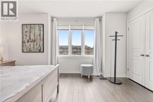 Bright primary bedroom featuring expansive windows with panoramic vistas, wood-finish flooring throughout, marble-topped bed frame, and direct access to a walk-in closet - 4171 Palermo Common, Burlington, ON - Indoor Photo Showing Bedroom