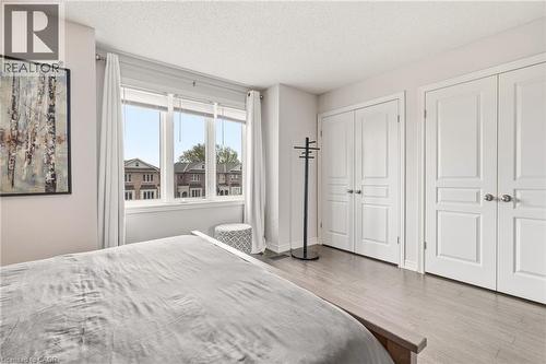 Large window with white trim, two sets of white double closet doors, and wood-finish flooring - 4171 Palermo Common, Burlington, ON - Indoor Photo Showing Bedroom
