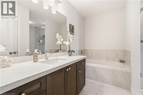 Integrated soaking tub, wood-finish vanity with ample storage, large rectangular mirror, and tiled flooring - 4171 Palermo Common, Burlington, ON - Indoor Photo Showing Bathroom