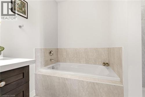 Spa-inspired primary bathroom featuring a recessed soaking tub with tile surround, dual wall-mounted faucets, and a dark wood vanity with integrated sink - 4171 Palermo Common, Burlington, ON - Indoor Photo Showing Bathroom