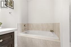 Spa-inspired primary bathroom featuring a recessed soaking tub with tile surround, dual wall-mounted faucets, and a dark wood vanity with integrated sink - 