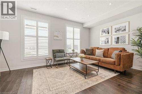 Bright living space featuring hardwood flooring throughout, plantation shutters framing dual windows, and a warm caramel leather sofa - 4171 Palermo Common, Burlington, ON - Indoor Photo Showing Living Room