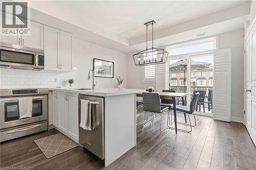 Contemporary kitchen and dining area featuring white cabinetry with brushed metal hardware, stainless steel appliances including a double wall oven, quartz countertops, and a large waterfall-edge isla - 4171 Palermo Common, Burlington, ON - Indoor Photo Showing Kitchen
