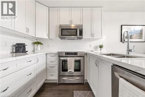 Modern kitchen featuring white shaker-style cabinetry with brushed nickel hardware, stainless steel appliances including a slide-in range and over-the-range microwave, white subway tile backsplash, an - 4171 Palermo Common, Burlington, ON - Indoor Photo Showing Kitchen With Stainless Steel Kitchen With Double Sink With Upgraded Kitchen