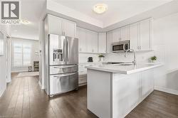 White shaker cabinetry, stainless steel appliances, white subway tile backsplash, white countertop, and wood-finish flooring - 