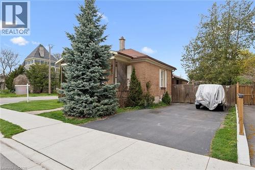 Brick exterior with a brown shingle roof, paved driveway, mature conifer, and wood fencing - 27 Roseview Avenue, Cambridge, ON - Outdoor