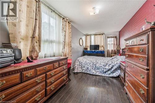 Wood-finish flooring with a contrasting brick-textured accent wall - 27 Roseview Avenue, Cambridge, ON - Indoor Photo Showing Bedroom