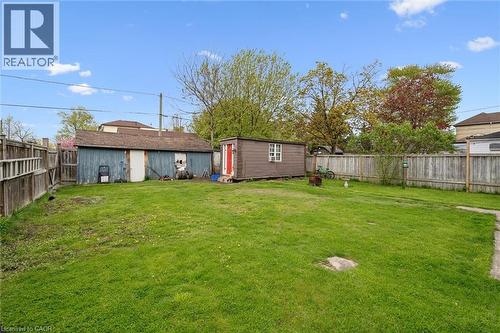 Expansive green lawn with a wooden privacy fence, featuring a large detached shed and an additional outdoor storage shed - 27 Roseview Avenue, Cambridge, ON - Outdoor With Backyard
