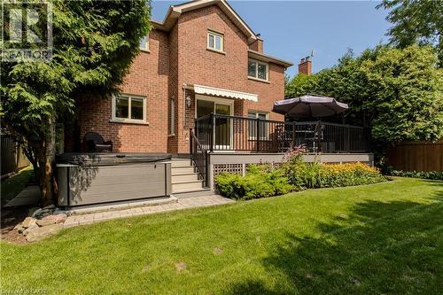 Brick exterior featuring an elevated deck with black railings, a hot tub, and a manicured lawn with garden beds - 1238 Sable Drive, Burlington, ON - Outdoor With Deck Patio Veranda