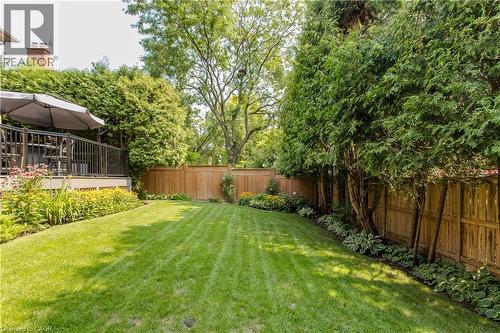 Expansive backyard featuring a manicured lawn, established garden beds, a wood privacy fence, and a raised composite deck with black railings - 1238 Sable Drive, Burlington, ON - Outdoor With Backyard