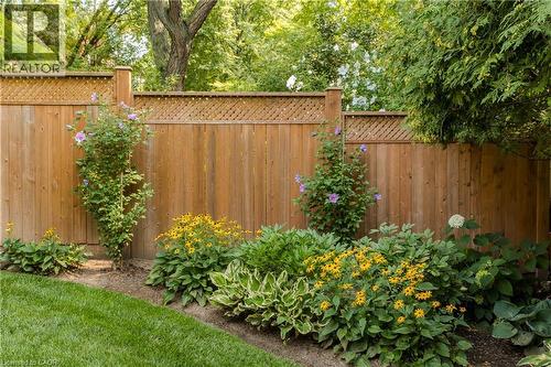 Wood privacy fence with lattice top, bordered by a planted garden bed featuring various mature shrubs, flowering plants, and hostas - 1238 Sable Drive, Burlington, ON - Outdoor
