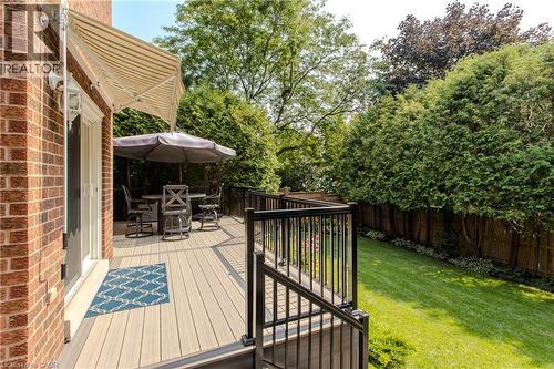 Brick exterior featuring a composite deck with black metal railings, a sliding glass door, and a retractable awning overlooking a manicured lawn - 1238 Sable Drive, Burlington, ON - Outdoor With Deck Patio Veranda