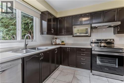 Dark wood cabinetry with brushed nickel hardware, white tiled flooring, stainless steel appliances, white subway tile backsplash, and a double basin sink with a gooseneck faucet - 1238 Sable Drive, Burlington, ON - Indoor Photo Showing Kitchen With Double Sink