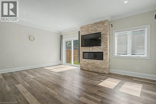Engineered wood flooring, stone-clad fireplace, built-in linear electric fireplace, crown molding, and sliding glass door - 31 Fourth Avenue, Kitchener, ON - Indoor Photo Showing Living Room With Fireplace