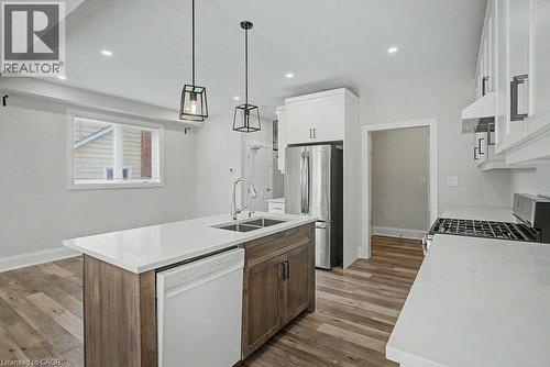 Kitchen featuring an island with double basin sink, white countertops, wood-finish flooring, stainless steel appliances, and white cabinetry - 31 Fourth Avenue, Kitchener, ON - Indoor Photo Showing Kitchen With Double Sink