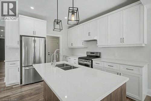 White shaker-style cabinetry, stainless steel appliances, central island with double basin sink, light-toned countertops, and wood-finish flooring - 31 Fourth Avenue, Kitchener, ON - Indoor Photo Showing Kitchen With Double Sink With Upgraded Kitchen