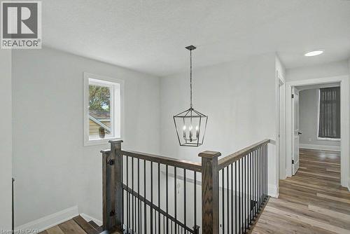 Hardwood-finish flooring, staircase with dark wood newel posts and metal spindles, recessed lighting, white trim, and a contemporary hanging light fixture - 31 Fourth Avenue, Kitchener, ON - Indoor Photo Showing Other Room