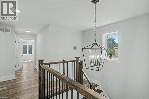 Hardwood-finish flooring, recessed ceiling lighting, a modern geometric chandelier, and a wood and metal stair railing - 31 Fourth Avenue, Kitchener, ON - Indoor Photo Showing Other Room