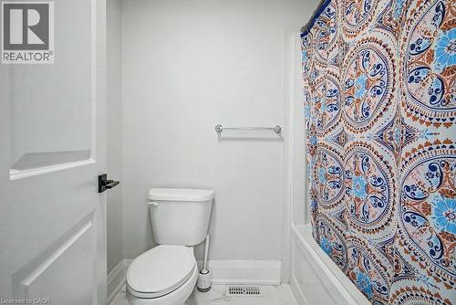 White paneled door with matte black hardware, white two-piece toilet, and a bathtub with white tile surround - 31 Fourth Avenue, Kitchener, ON - Indoor Photo Showing Bathroom
