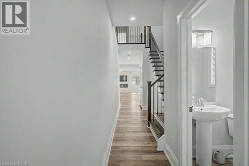 Hardwood-finish flooring, staircase with dark wood treads and wrought iron balusters, recessed lighting, and a pedestal sink with a contemporary light fixture - 31 Fourth Avenue, Kitchener, ON - Indoor