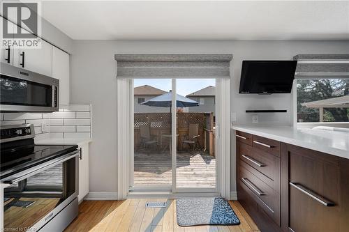 Hardwood-finish flooring, white subway tile backsplash, stainless steel appliances, dark wood-finish cabinetry, and a sliding glass door to an outdoor deck - 57 Grindstone Way, Waterdown, ON - Indoor Photo Showing Kitchen