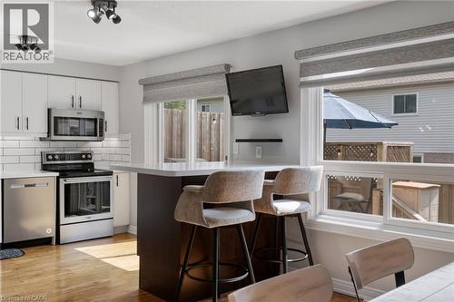 Contemporary kitchen featuring a peninsula with seating, stainless steel appliances, white subway tile backsplash, and wood-finish flooring - 57 Grindstone Way, Waterdown, ON - Indoor Photo Showing Kitchen With Stainless Steel Kitchen