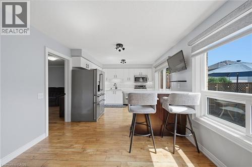 Wood-finish flooring throughout, bright white walls, modern kitchen with white cabinetry, stainless steel appliances, and a central island with bar seating - 57 Grindstone Way, Waterdown, ON - Indoor