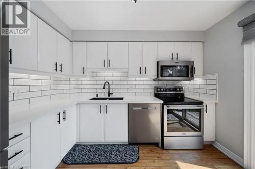 Modern kitchen featuring white cabinetry, black hardware, stainless steel appliances, white subway tile backsplash, and wood-finish flooring - 57 Grindstone Way, Waterdown, ON - Indoor Photo Showing Kitchen With Stainless Steel Kitchen With Double Sink