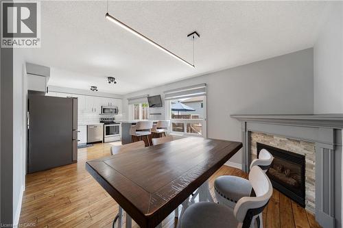 Wood-finish flooring, built-in fireplace with stone-look surround, white kitchen cabinetry, stainless steel appliances, and a kitchen island with seating - 57 Grindstone Way, Waterdown, ON - Indoor Photo Showing Dining Room