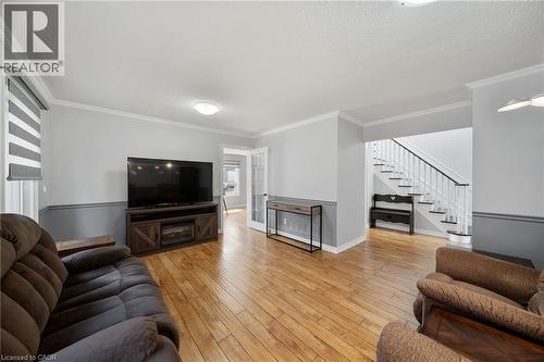 Hardwood-style flooring throughout, crown molding, two-tone wall treatment, built-in media console with fireplace feature, and white wood staircase with dark handrail - 57 Grindstone Way, Waterdown, ON - Indoor Photo Showing Living Room