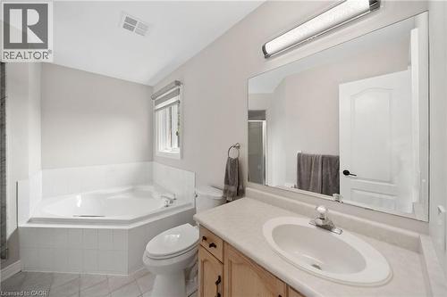 Corner soaking tub with white tile surround, single vanity with integrated sink, and large wall-mounted mirror - 57 Grindstone Way, Waterdown, ON - Indoor Photo Showing Bathroom