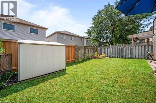 Expansive backyard featuring a lush, manicured lawn with mature shade trees, vinyl privacy fencing, and a detached storage shed with wood-finish siding and white trim - 57 Grindstone Way, Waterdown, ON - Outdoor