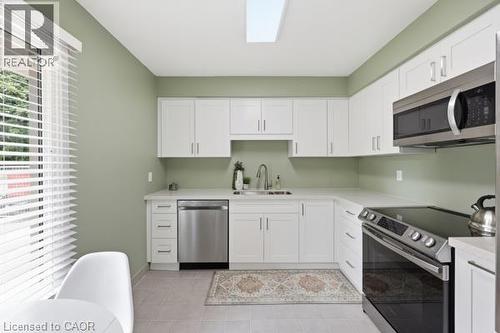 White cabinetry with brushed nickel hardware, stainless steel appliances, light-toned countertop, skylight, and tile flooring - 15 Green Valley Drive Unit# 41, Kitchener, ON - Indoor Photo Showing Kitchen With Double Sink