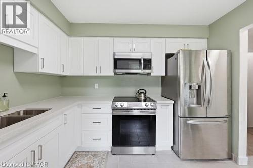 White cabinetry with brushed nickel hardware, stainless steel appliances, dual basin sink, light-toned countertops, and light-toned tile flooring - 15 Green Valley Drive Unit# 41, Kitchener, ON - Indoor Photo Showing Kitchen With Double Sink