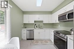White cabinetry with brushed nickel hardware, stainless steel appliances, light-toned countertop, skylight, and tile flooring - 