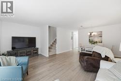 Wood-finish flooring throughout, bright white walls, recessed staircase with carpeted treads, and a dining area featuring a chandelier - 