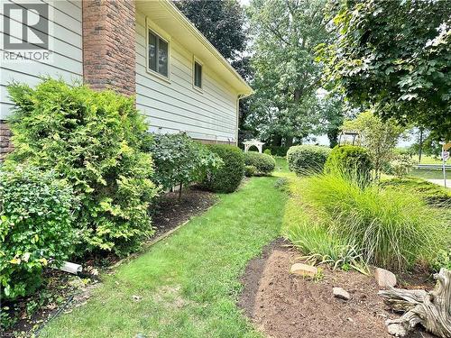 Siding exterior with brick chimney accent, manicured shrubs, mature trees, and a landscaped garden bed - 44 Douglas Avenue, Simcoe, ON - Outdoor