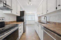 Kitchen featuring white cabinetry, stainless steel appliances, a double basin sink, and a range with overhead ventilation - 
