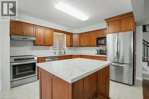 Kitchen featuring a central island with a quartz countertop, Maple wood cabinetry, stainless steel appliances, and a tiled backsplash - 568 Robert Ferrie Drive, Kitchener, ON - Indoor Photo Showing Kitchen