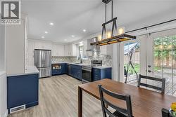 Contemporary kitchen featuring two-tone cabinetry, stainless steel appliances, a mosaic tile backsplash, wood-finish flooring, and a linear chandelier - 